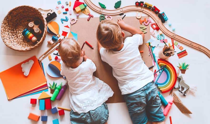 Zwei kleinere Kinder liegen auf dem Boden und sind umgeben mit diversen Spielsachen